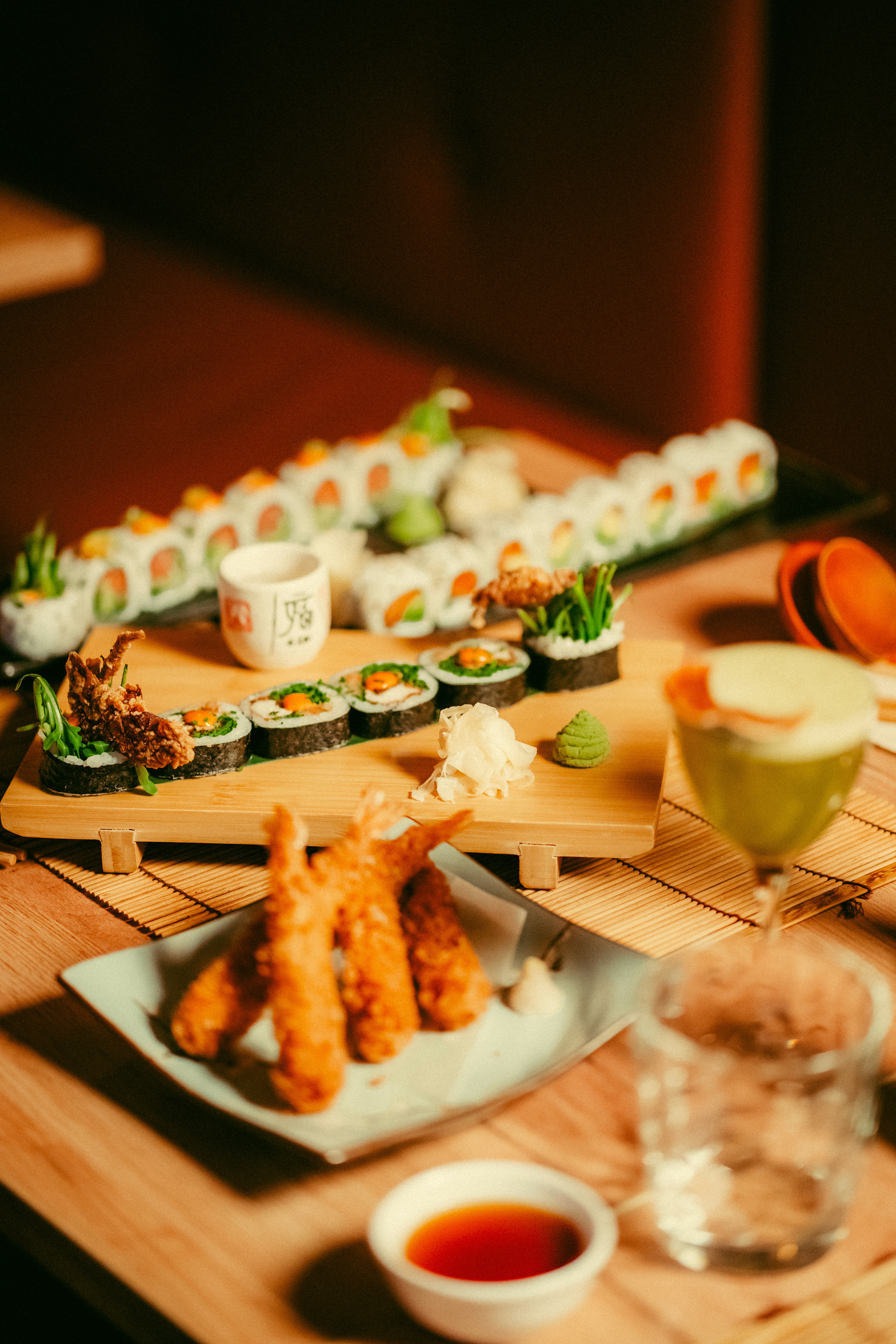 remium bottomless sushi and cocktails at East London's No.1 Japanese restaurant. A wooden platter of signature sushi rolls and a green matcha cocktail, part of a £49 unlimited dining experience in London