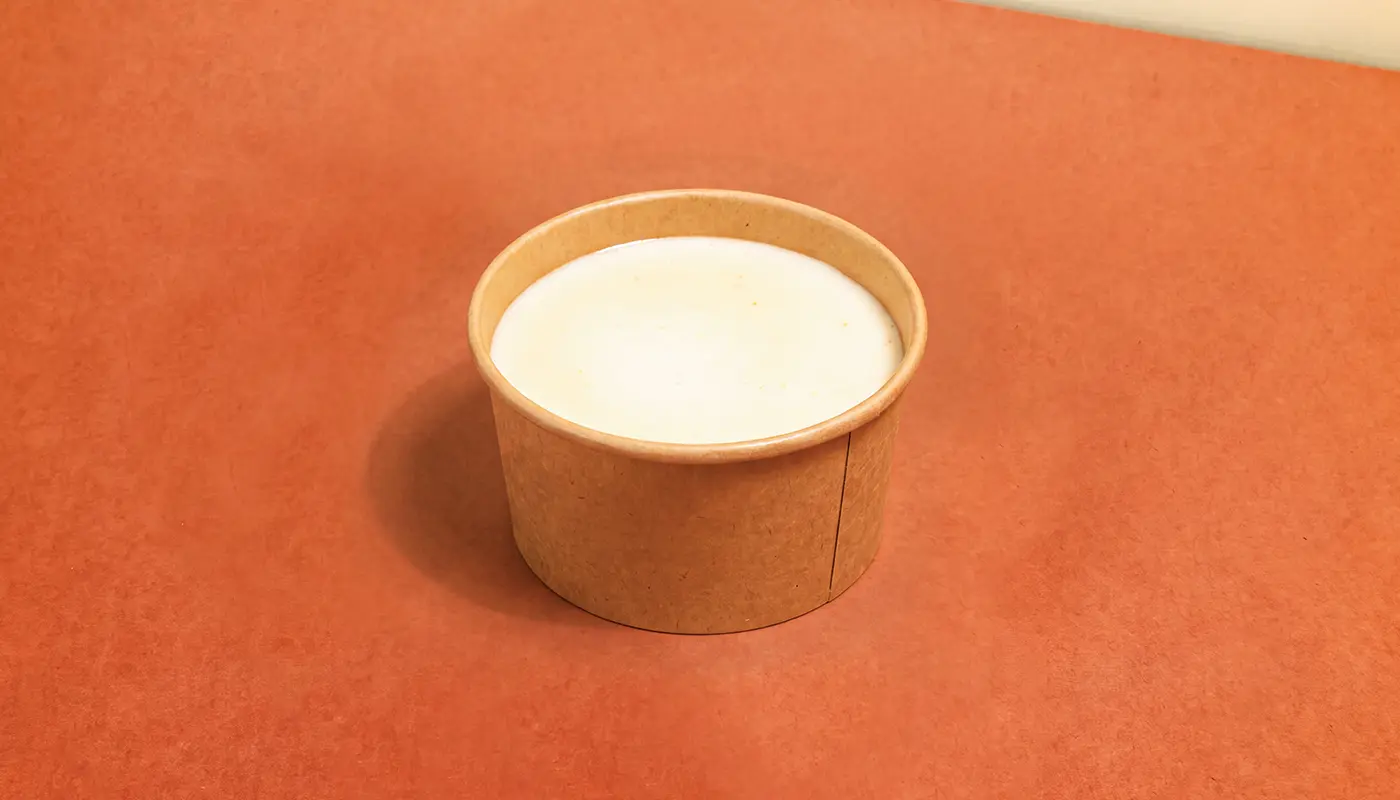 A small kraft-paper cup filled with smooth pale queso.