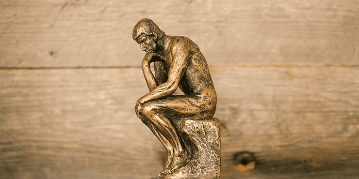 A bronze-colored miniature replica of Auguste Rodin’s sculpture, "The Thinker," positioned against a rustic, light-brown wooden background.