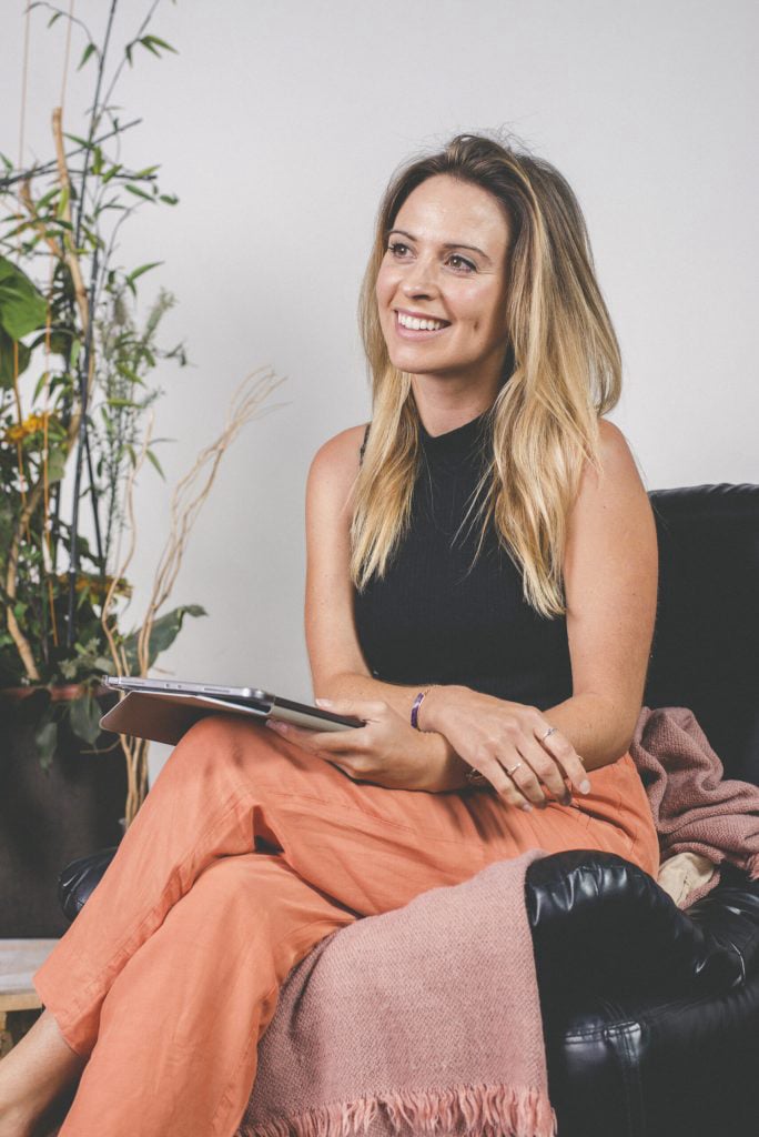 Smiling psychotherapist seated with a tablet in a bright, welcoming therapy setting.