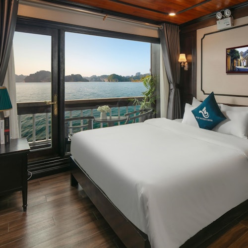 Et hyggeligt soveværelse med en hvid seng, natbord og et stort vindue med udsigt over havet og fjerne øer.