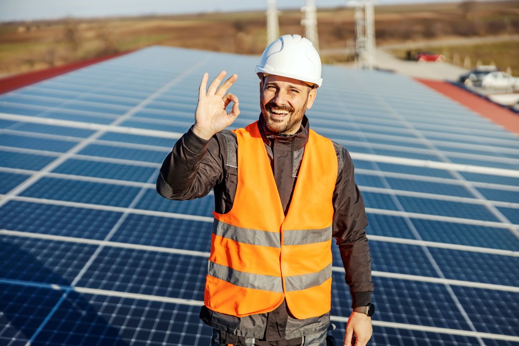 Techniker von Solartechnik Nordwest auf einem Solardach, trägt Sicherheitsweste und Helm, zeigt ein 'OK'-Zeichen – fachgerechte Installation von Photovoltaikanlagen für nachhaltige Energie.