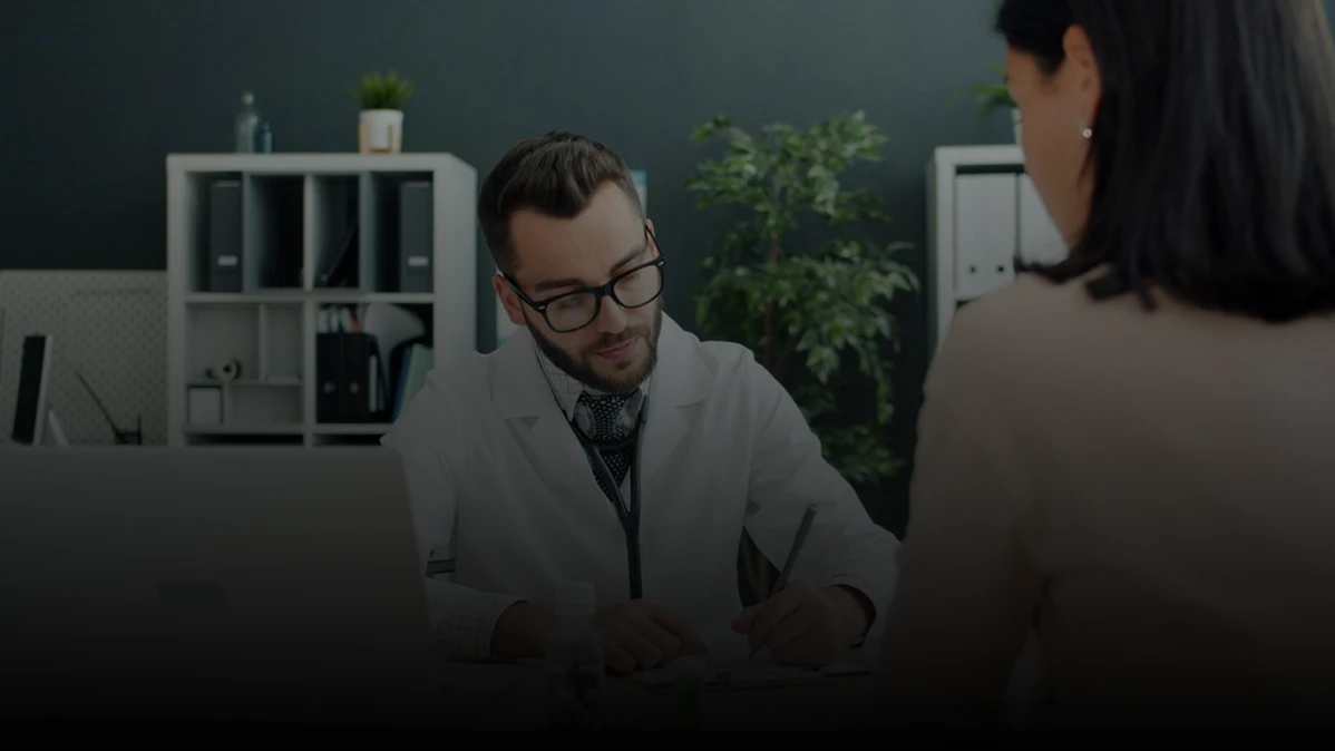 Doctor writing notes while patient sits opposite.