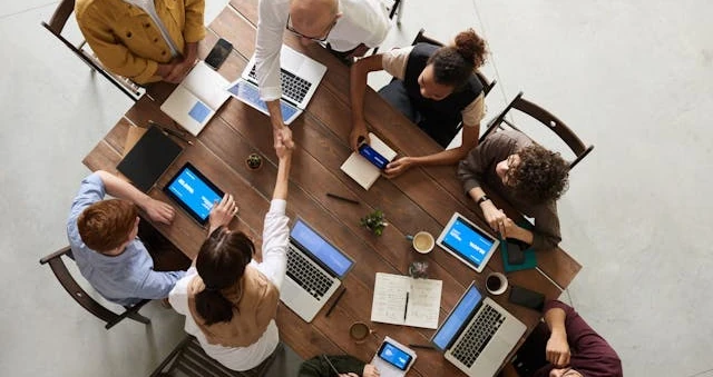Vista de cima de uma mesa comprida com várias pessoas trabalhando em laptops