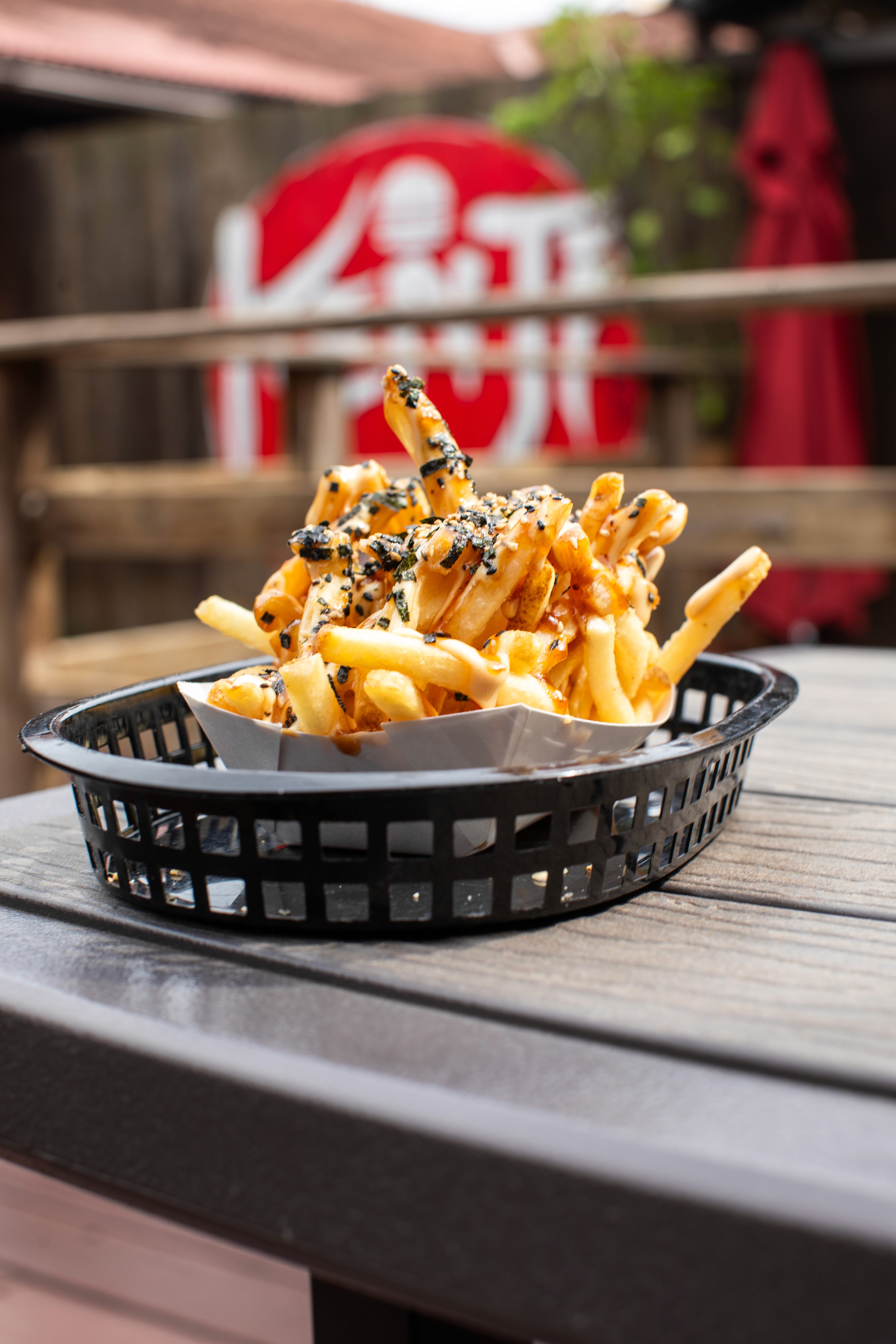A close-up of a rustic food spread featuring a small bowl filled with mixed green and black olives on a wooden board, with a bowl of yogurt or dip and a salad in the background.