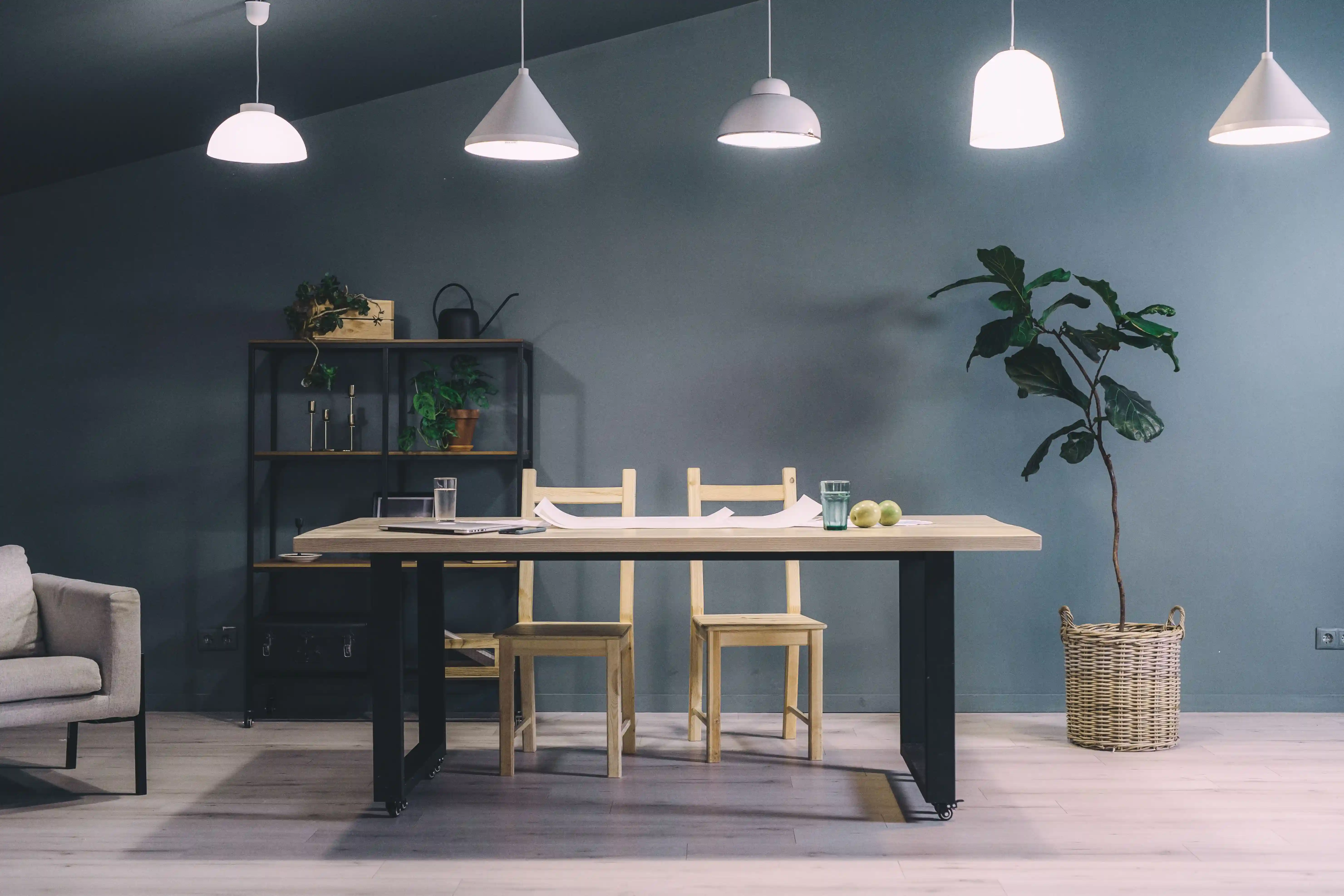 Minimalist home office setup with dark wall, wooden desk, illuminated table lamp, and plants.