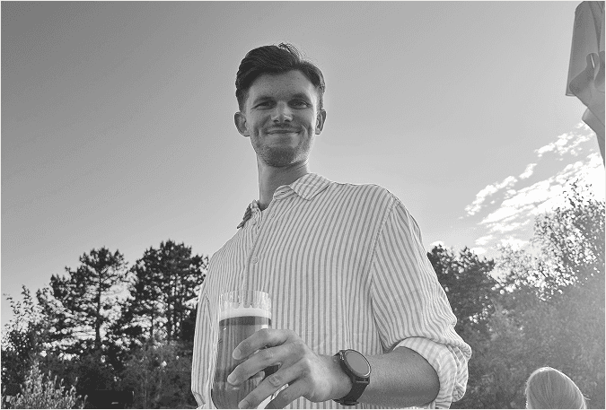 Black-and-white photo of a person standing outdoors, smiling and holding a drink.