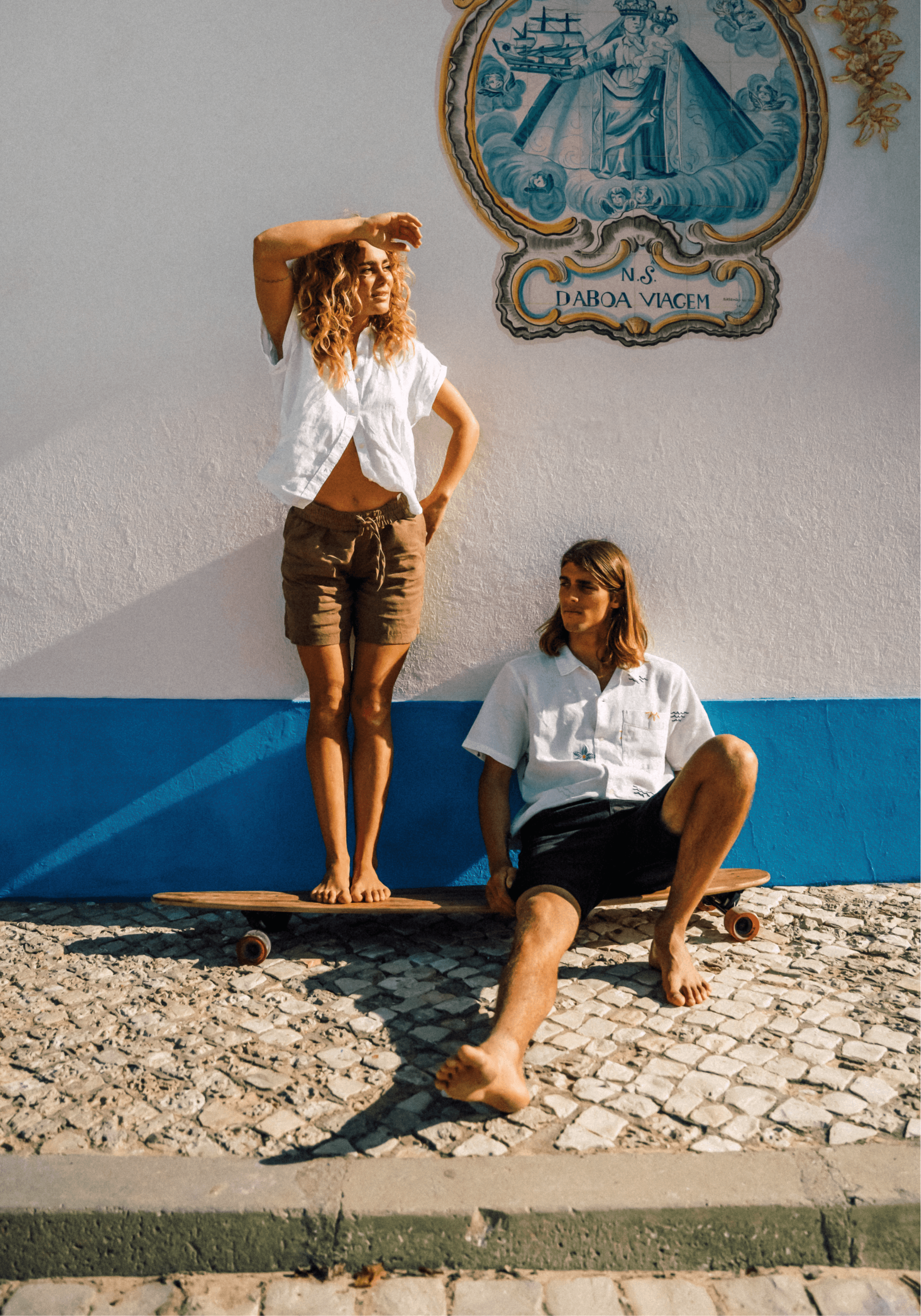 Deux filles en short et chemisette posent sur un skate devant une mosaique à l'effigie de la ville d'Ericeira