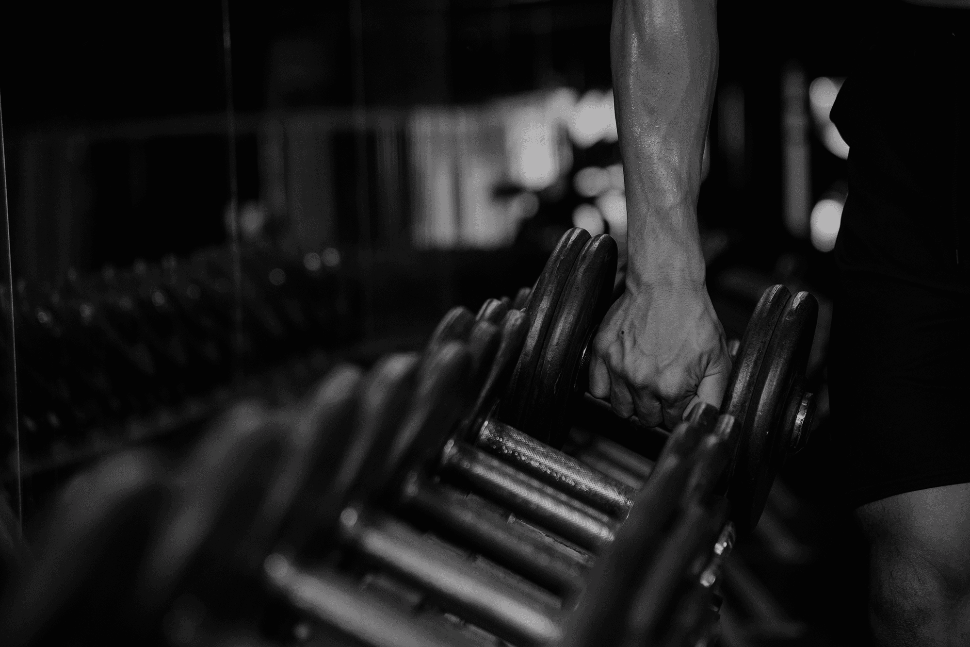 Close-up detail of athlete holding dumbbells during strength workout in gym.