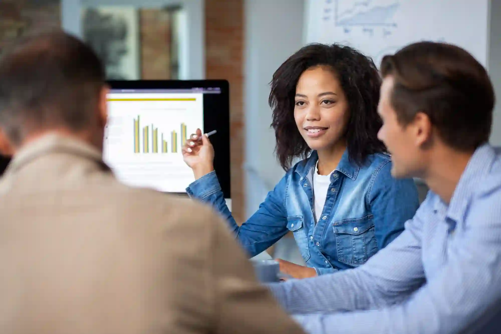 Diverse team collaborating around a computer screen, reviewing bar graphs for data-driven business strategy.