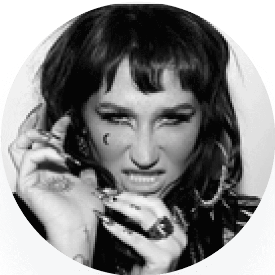Black and white portrait of Kesha, a woman with dark hair, making a fierce expression and holding their hand up.