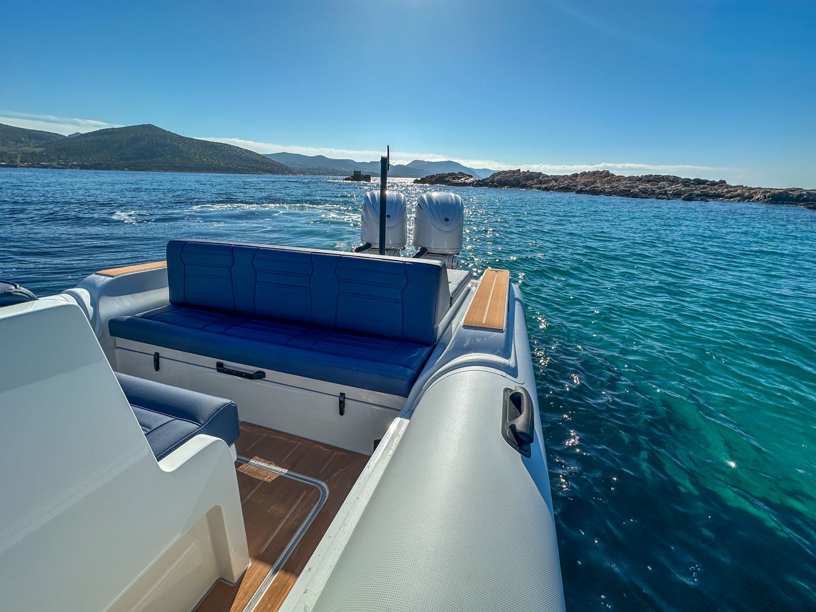 White Rock 36 speedboat with captain at helm cruising calm blue waters near Paros coastline with hills in background.