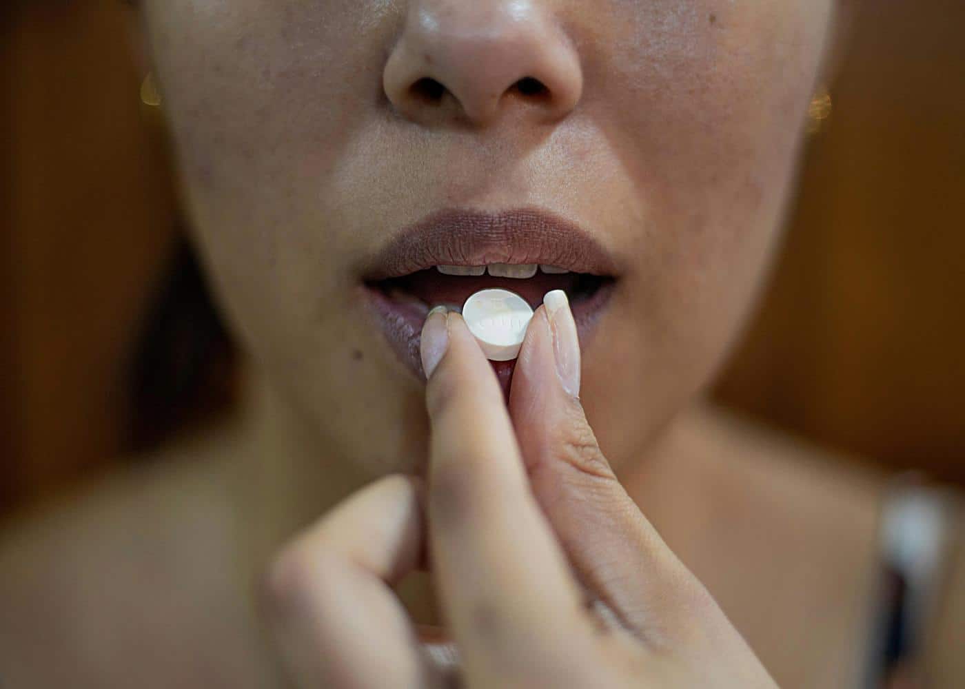 Woman preparing to swallow a round collagen supplement