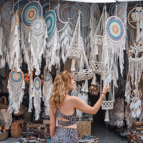 一個穿著花紋服裝的人正在商店裡看五顏六色的夢捕手和macramé物品的展示。