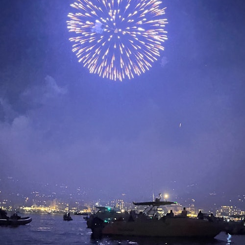 Fyrverkeri lyser opp nattehimmelen over bylandskapet og båtene på vannet.