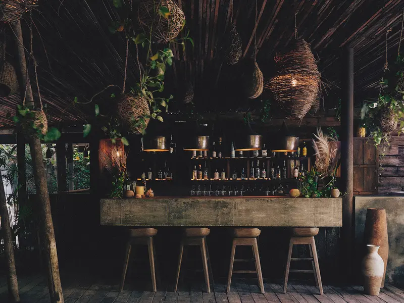 Jungle Bar en Be Tulum con un ambiente exuberante, asientos y exhibición de botellas de licor.