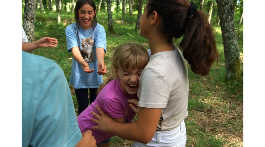 Bambini che giocano e si abbracciano durante un campo estivo in natura, sviluppando relazione, fiducia in sé e crescita personale