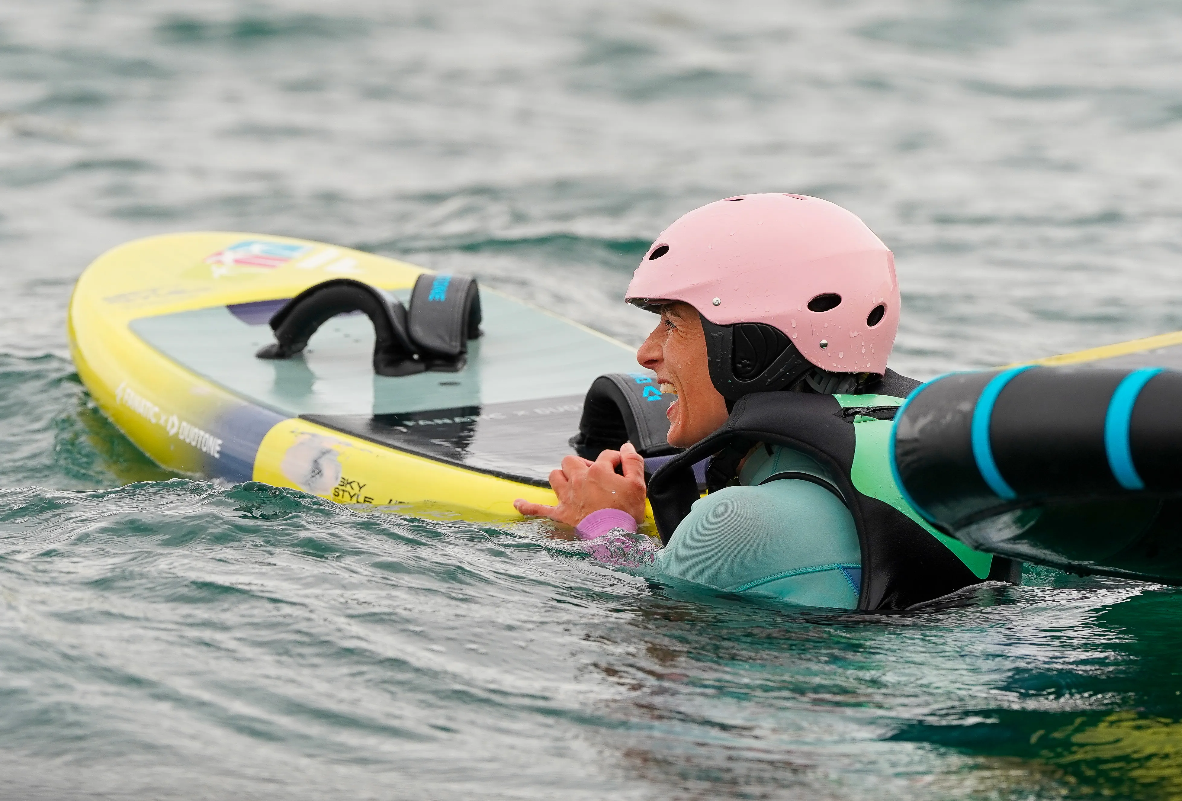 Une femme dans l'eau à côté de sa planche de wingfoil