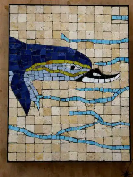 Colorful dolphin mosaic art piece with blue waves and sandy background.