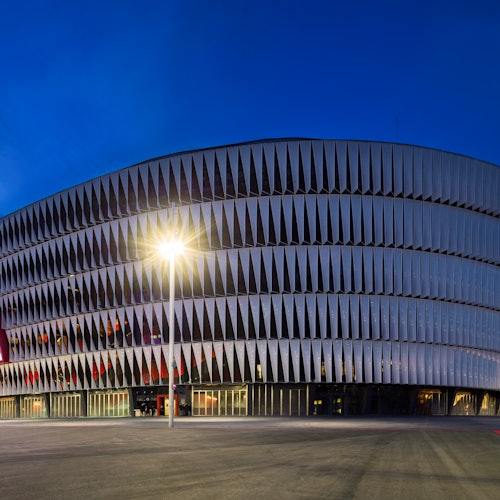 Modern multi-story building with unique vertical slats on the facade, illuminated by a streetlight at dusk.