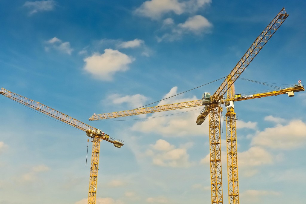 Gruas de construção civil em canteiro de obras, representando engenharia, infraestrutura e desenvolvimento imobiliário.