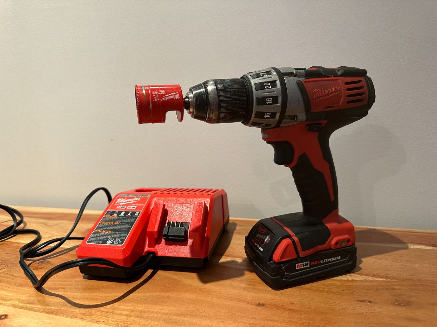Kit visseuse sans fil Milwaukee M18 avec scie cloche rouge de 1-3/8 pouces et chargeur, posé sur une table en bois à Montréal – Saint-Henri