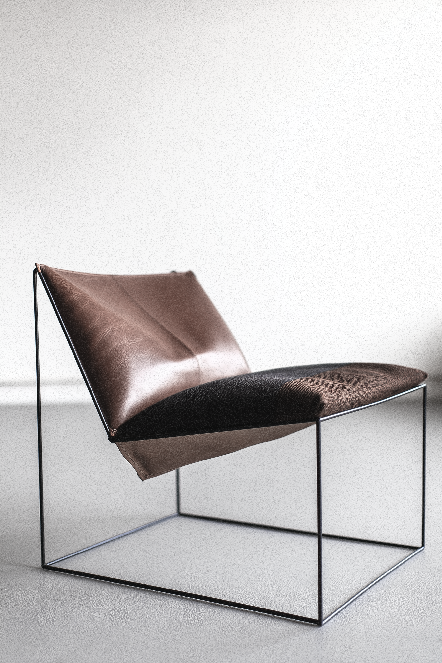 Minimal leather lounge chair with brown and black upholstery on a thin metal frame against a light background