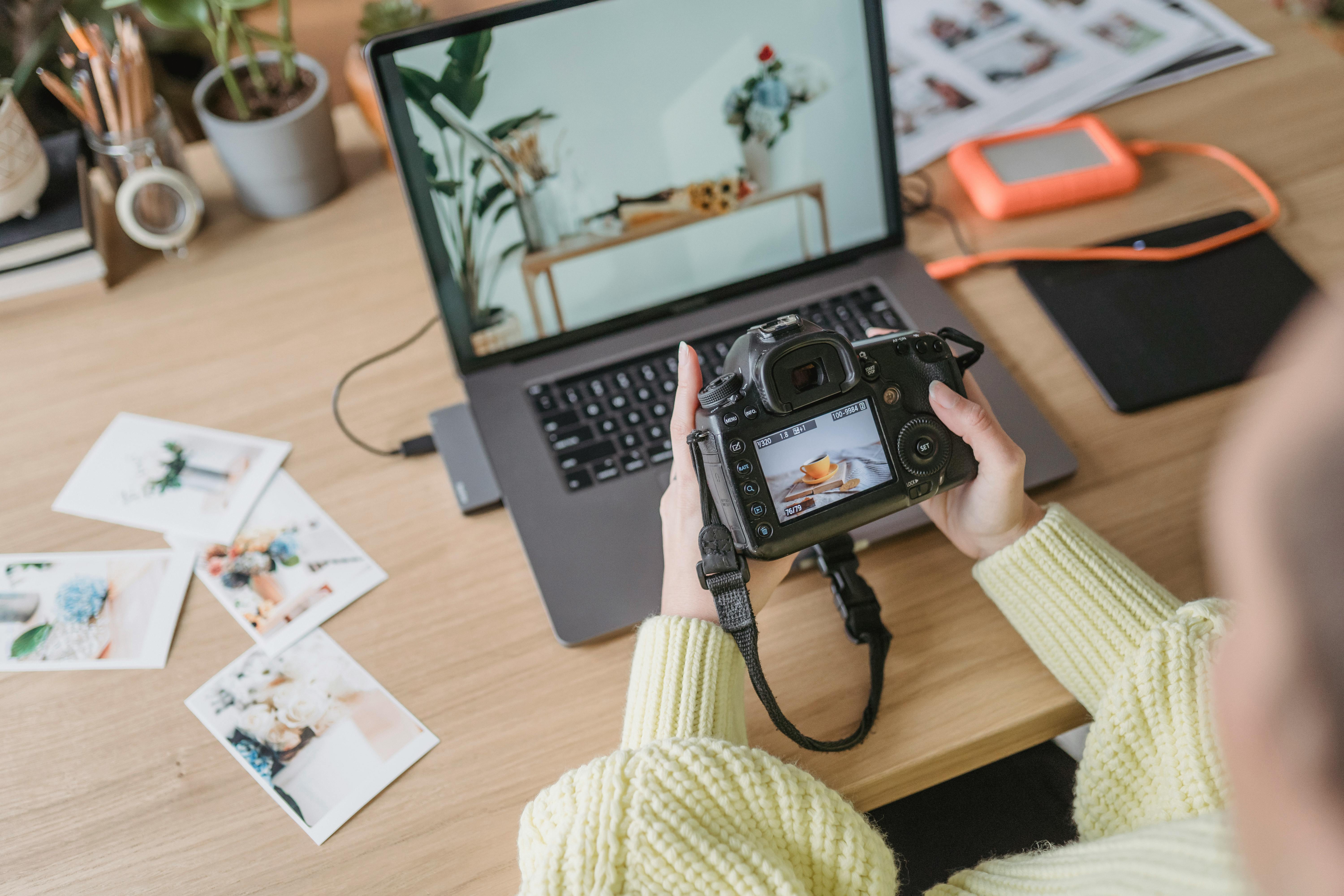 Photographer reviews camera shots on laptop with printed photos on desk.