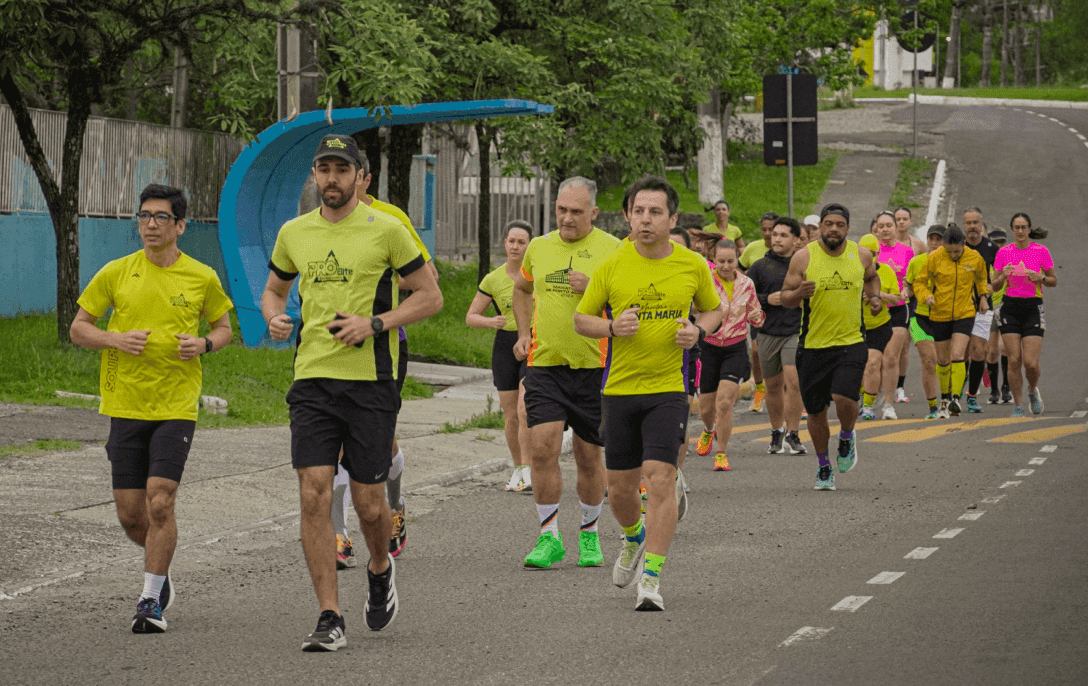 Grupo de alunos da Pro Elite Assessoria Esportiva correndo juntos em uma rua de parque arborizada, seguindo as orientações do treinador de corrida à frente.