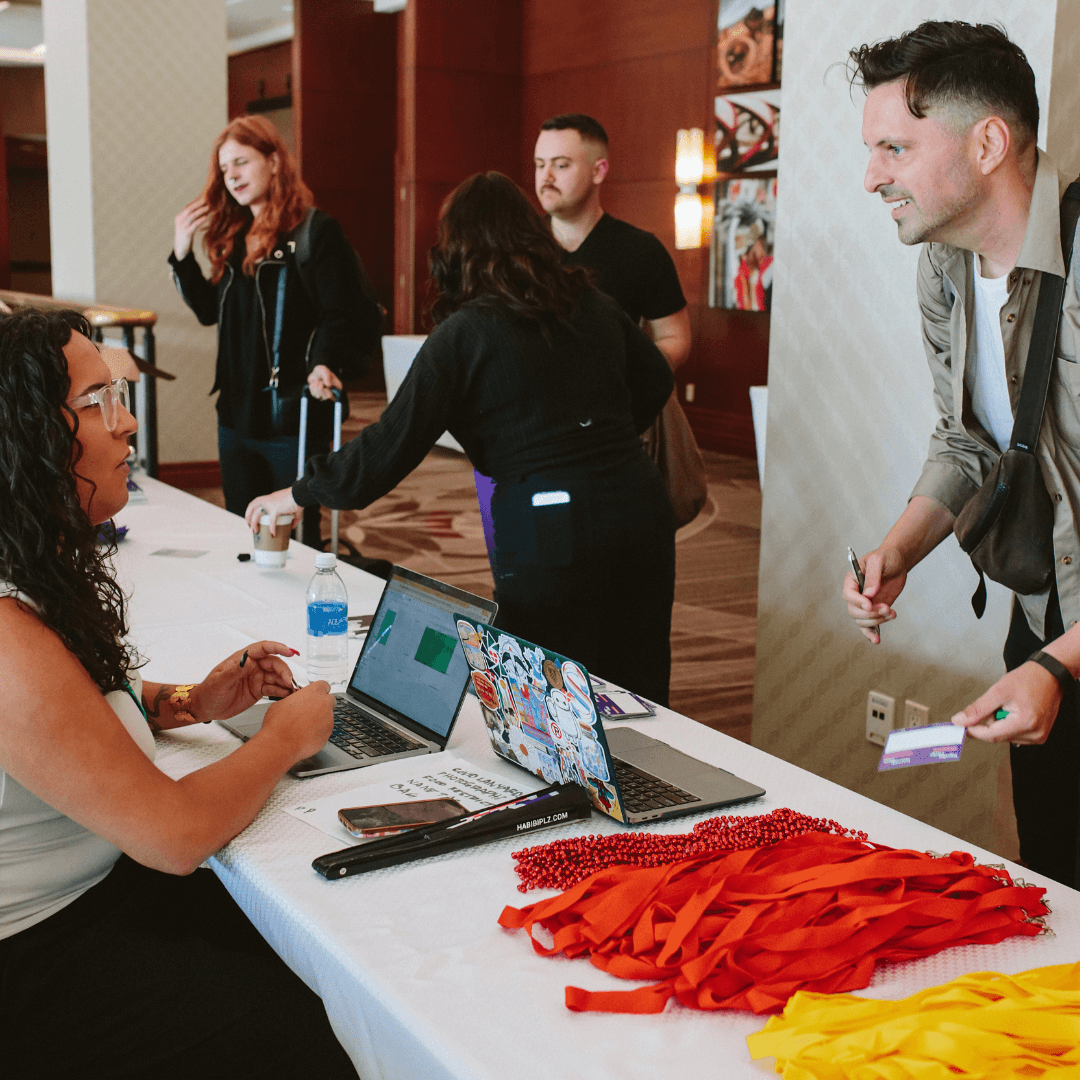 A registration desk with attendees checking in, colorful lanyards on the table, and staff assisting participants.