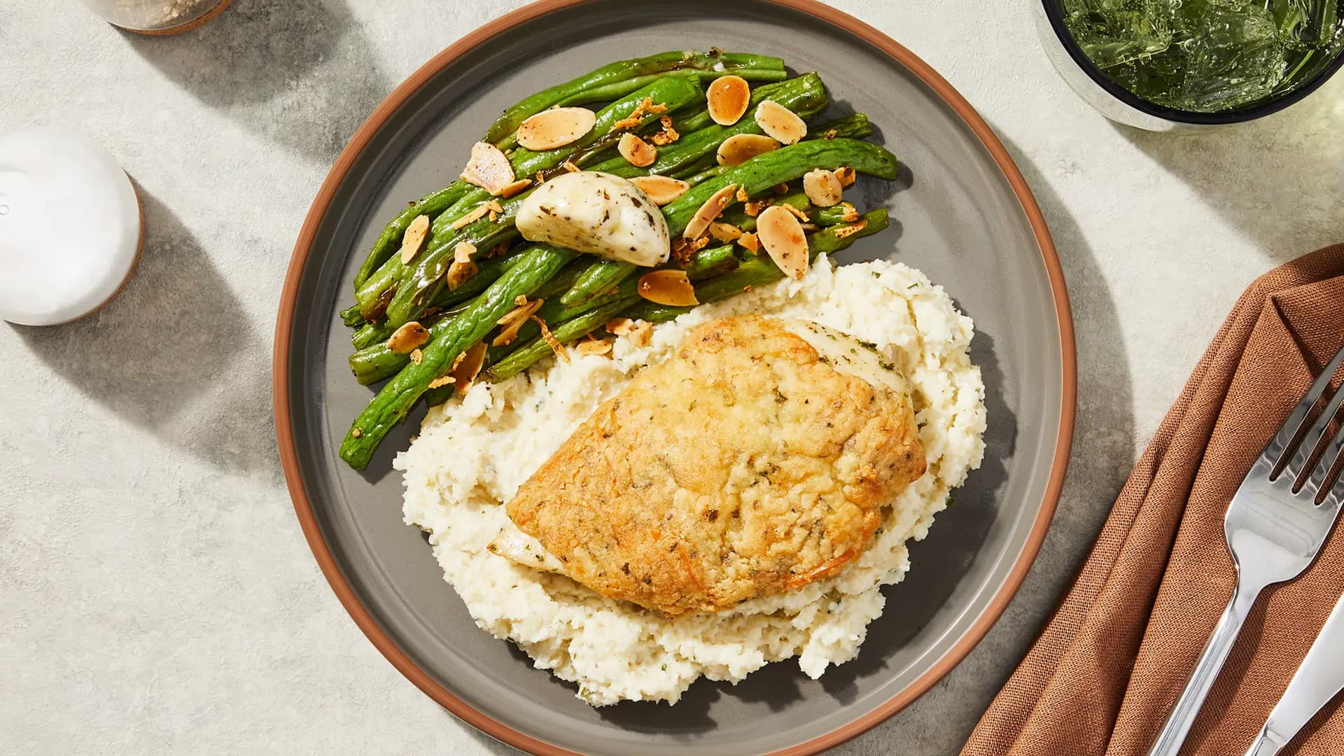 Proteinreiches Hähnchen mit Kräuterkruste, Blumenkohlreis und grünem Gemüse auf einem Teller angerichtet