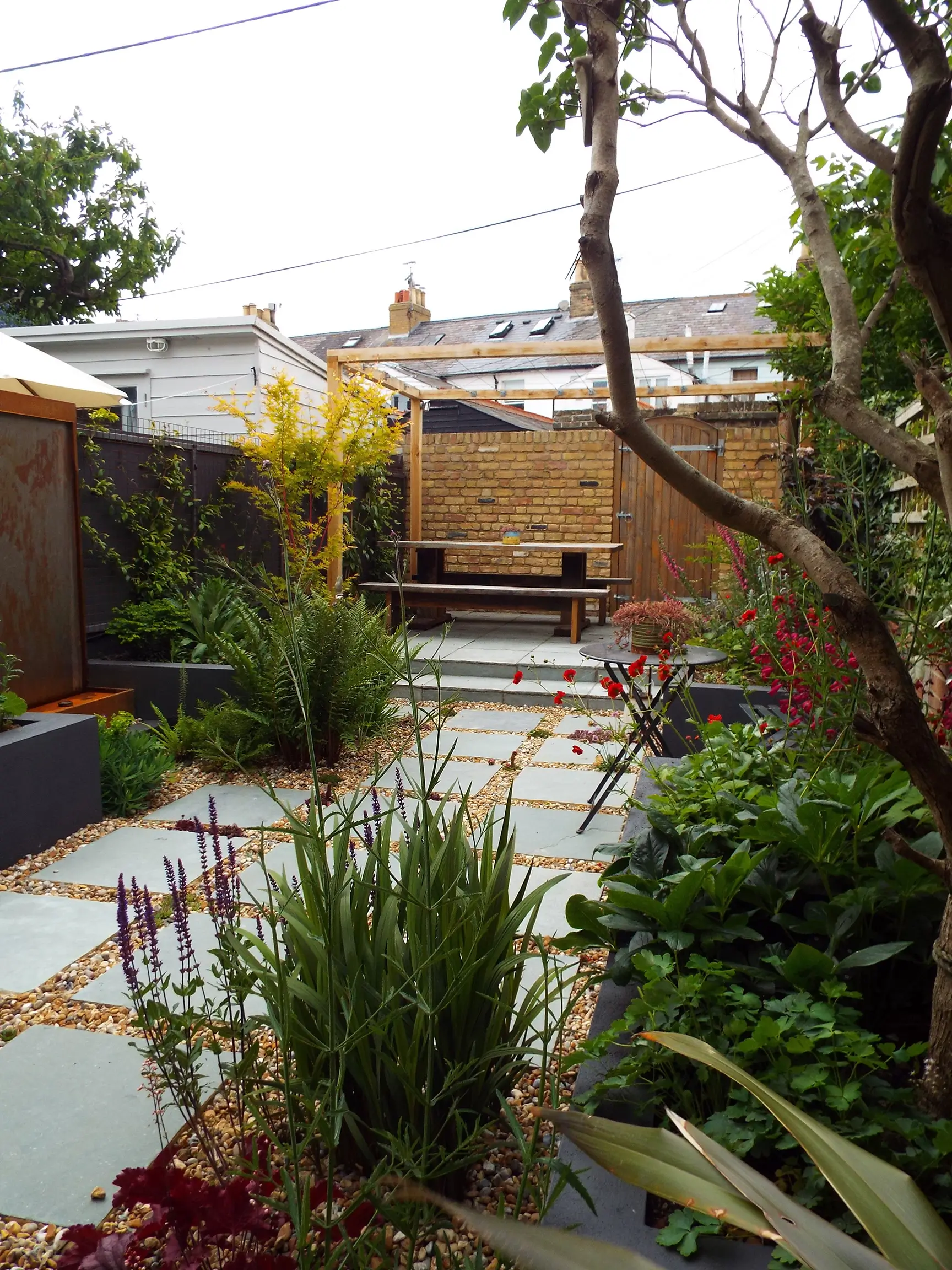 A serene garden view featuring stone pathways, lush plants, and a tranquil atmosphere under an overcast sky.