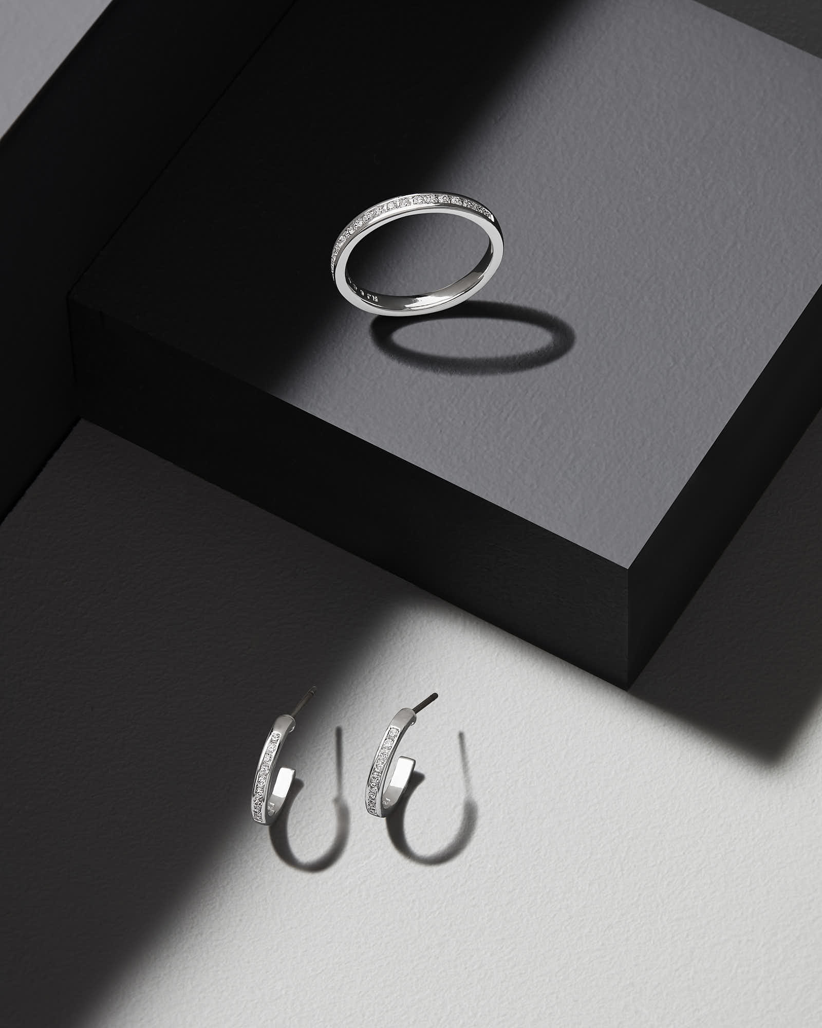 Silver earrings displayed on a minimalist background, featuring both hoops and circular designs.