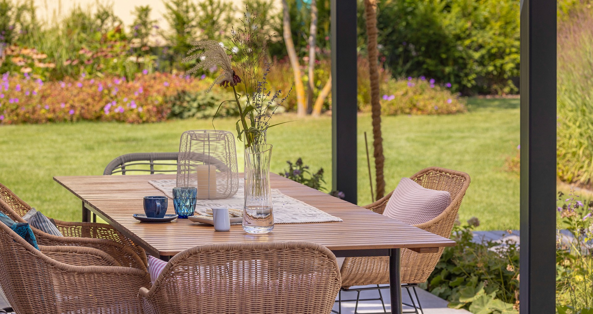 Überdachter Sitzbereich mit Blick in einen naturnah bepflanzten Garten mit Stauden und Gräsern.