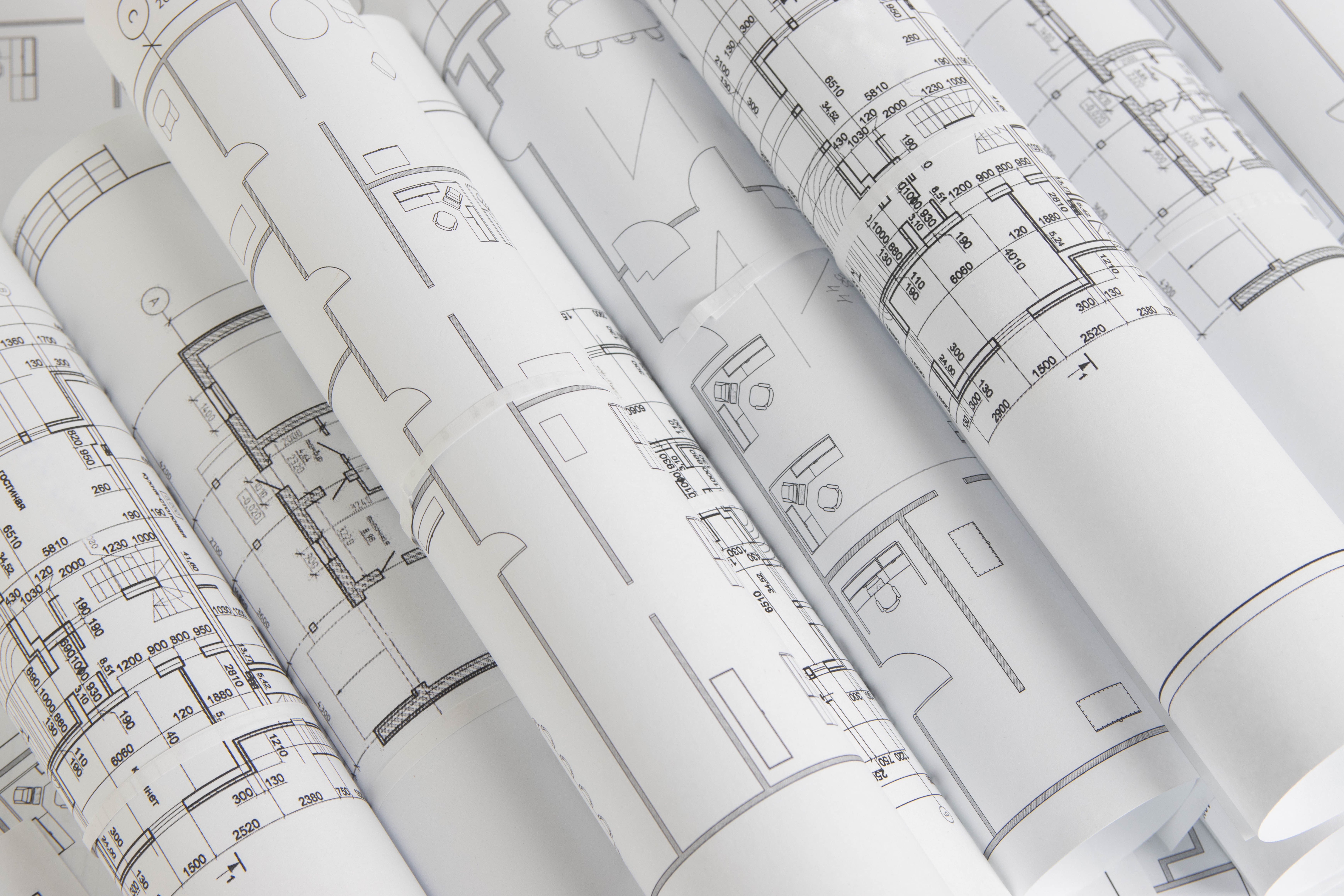 Rolled architectural blueprints with detailed floor plan drawings spread in overlapping layers.