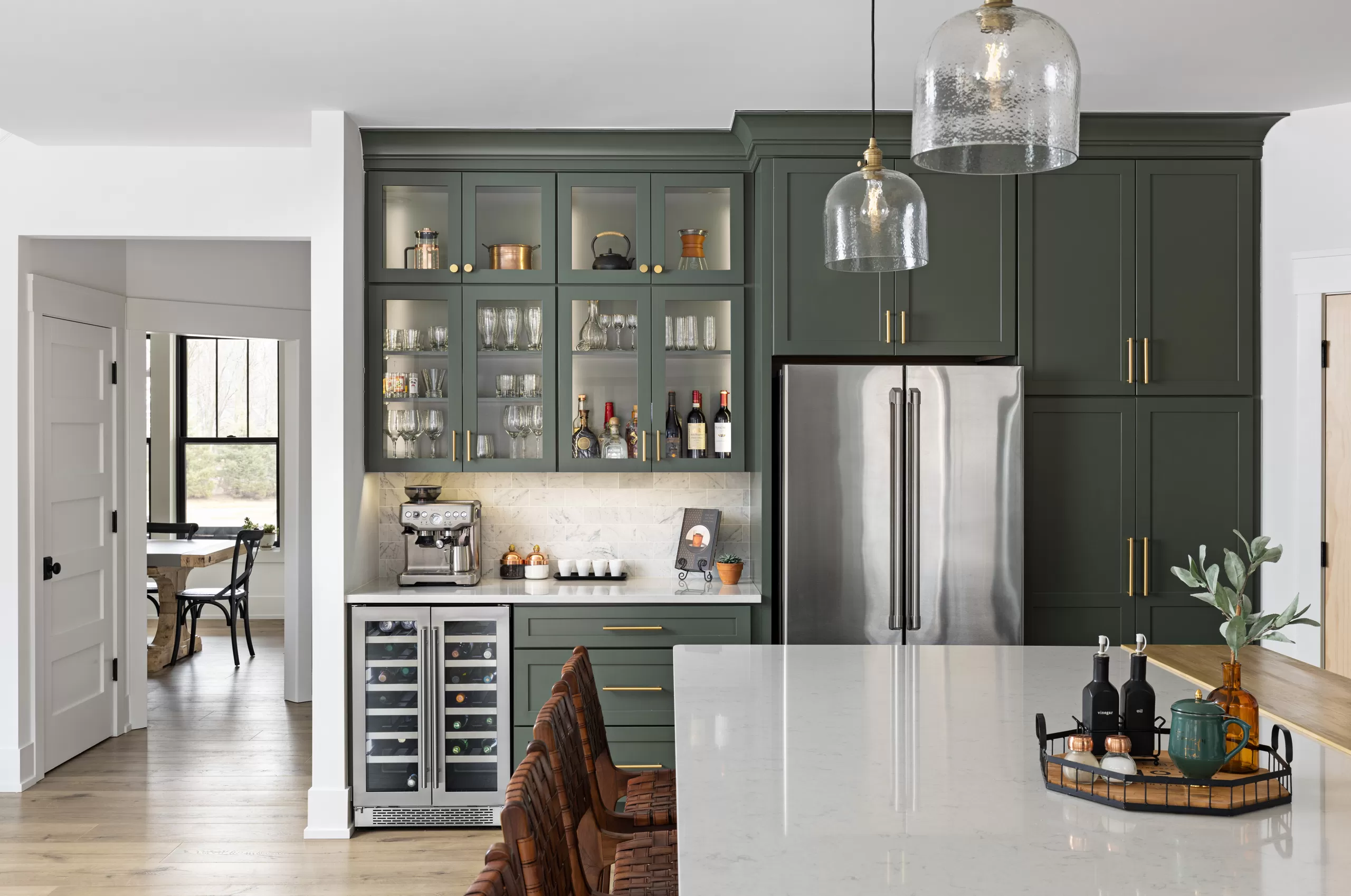 Dark green kitchen with glass-front display cabinets, a built-in wine fridge, and a glass pendant light, representing KSI's cabinets work.