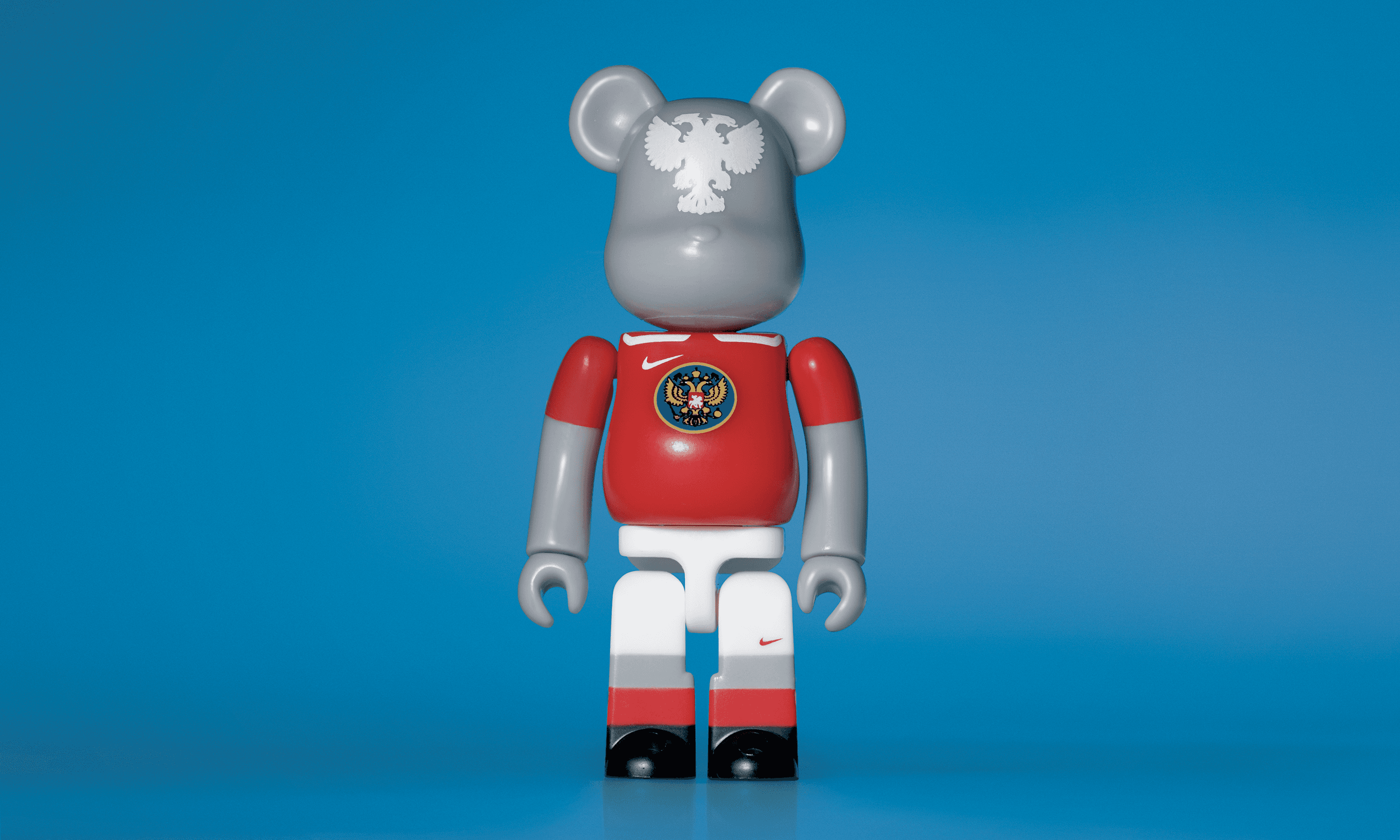 A single 3.5” tall Bre@rbrick/Nike toy created to commemorate the 2006 Russian World Cup football team. The toy is painted to appear in the Russian football kit and stands in the center of the frame in front of a blue background. 