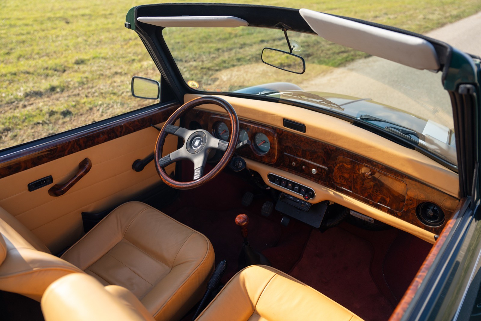Aerial view of a classic convertible car's interior featuring beige seats and wooden accents.
