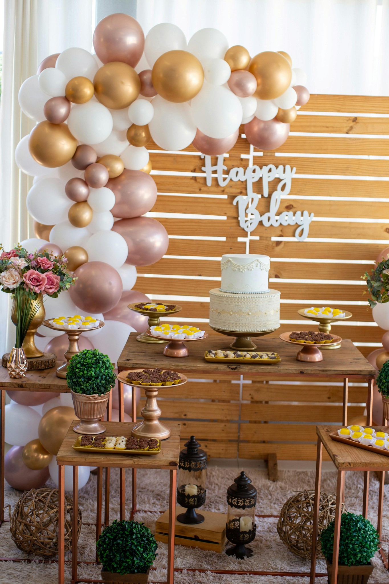 legant balloon and floral backdrop with gold, white, and beige balloons surrounding a cake table for a baby shower or birthday