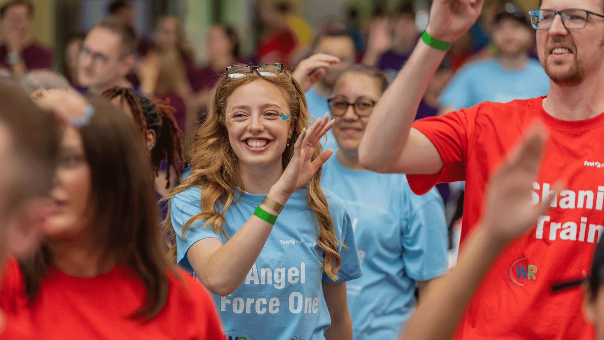 Outdoor team-building event with participants wearing matching blue shirts, taking part in inflatable obstacle courses and games, smiling and cheering, with the words 'ENTER A TEAM' in large bold white and green text across the image.