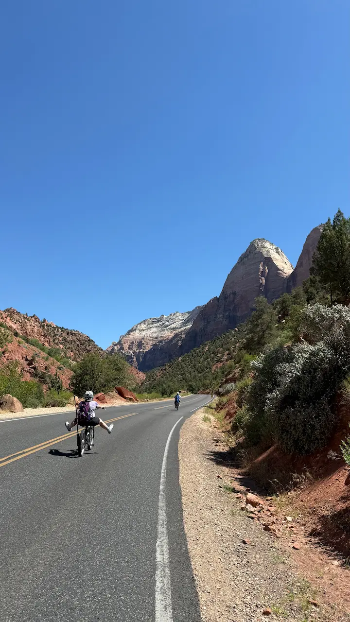 Stu and family riding bikes down a winding mountain road in Zion National Park—capturing motion, freedom, and the journey of living one mile at a time.