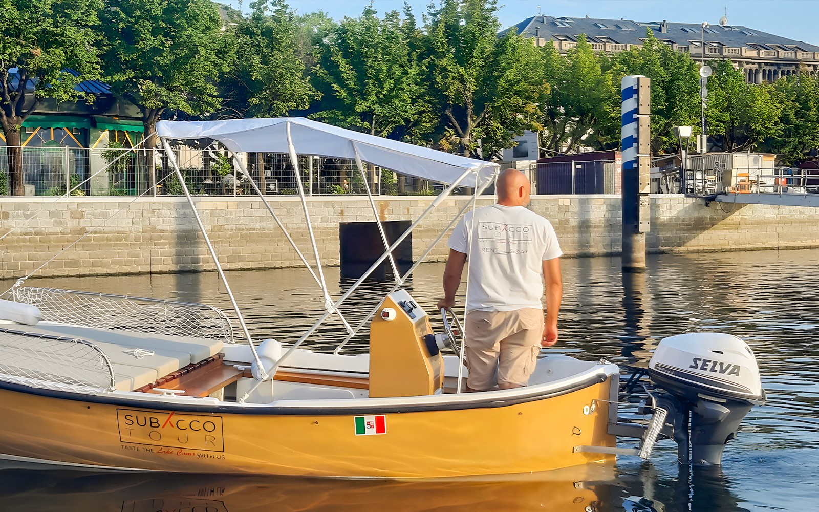 Boat rental on Lake Como with a person standing on a yellow boat near the shore.