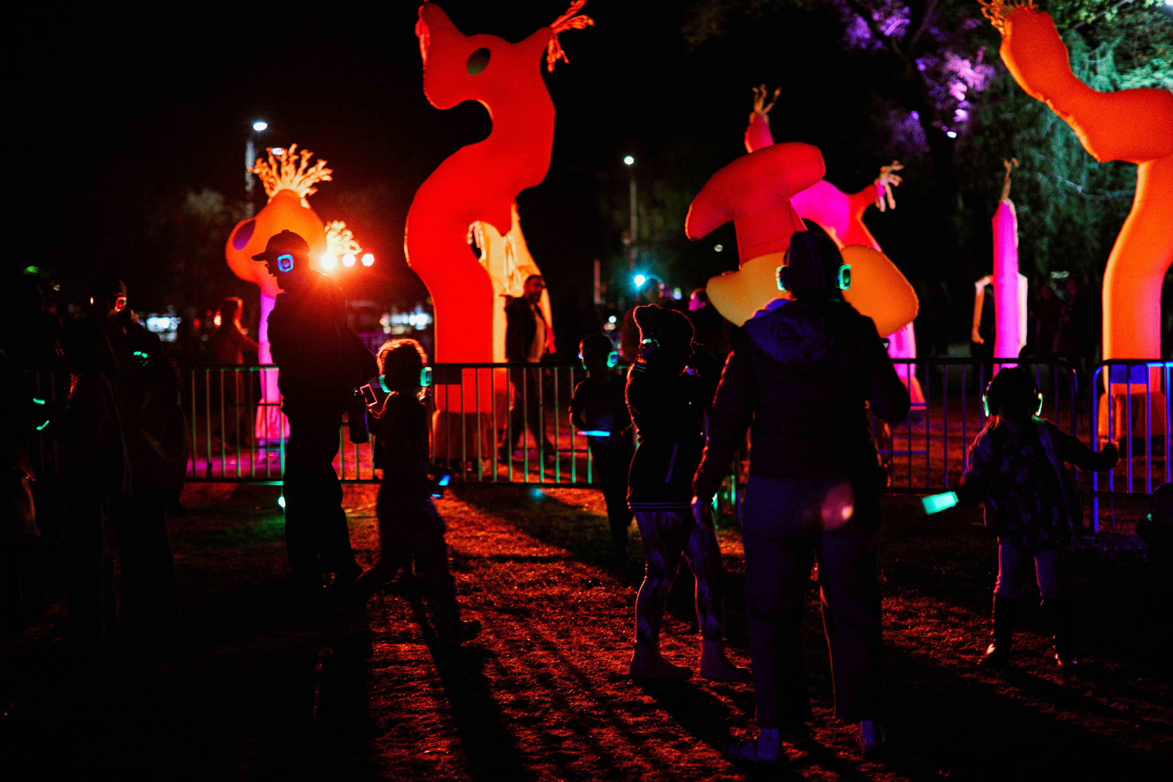 A group of people dancing to silent disco with brightly colored costumes performing against a dark, nighttime backdrop.