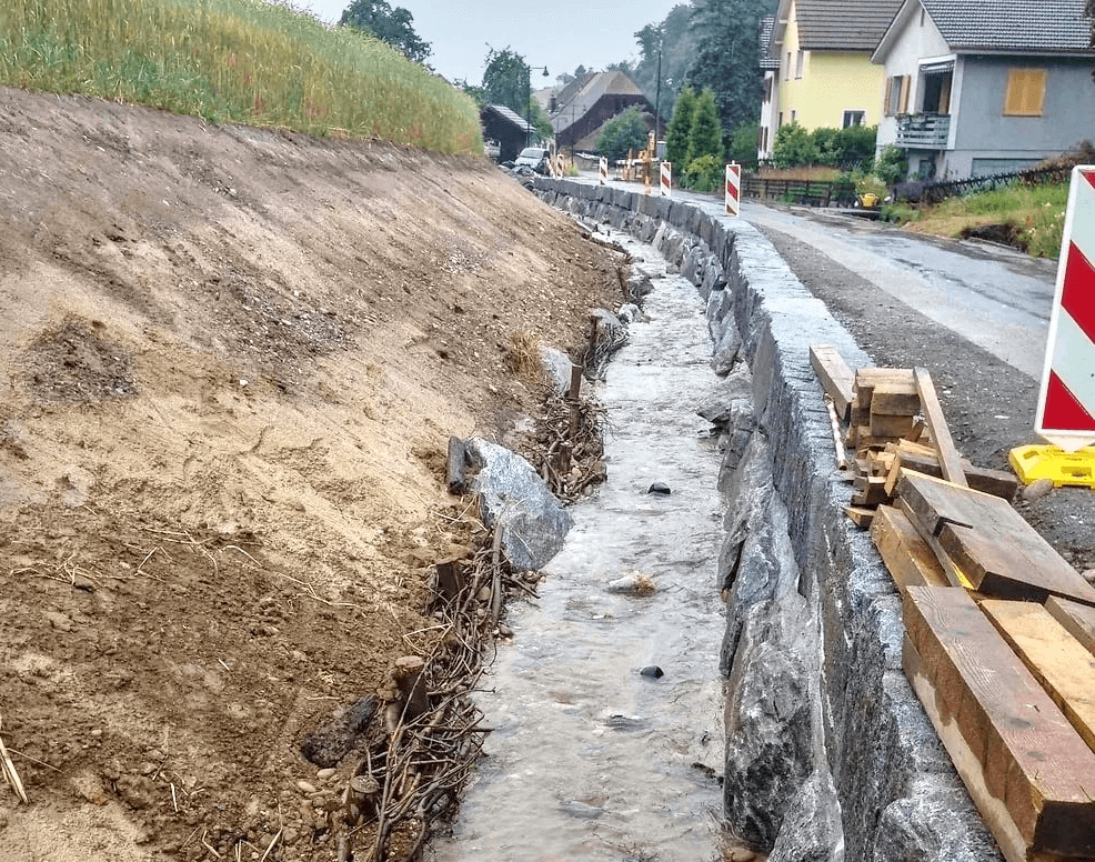 Roadside drainage channel under construction by Strub Bau AG – water management and erosion control infrastructure in a residential area.