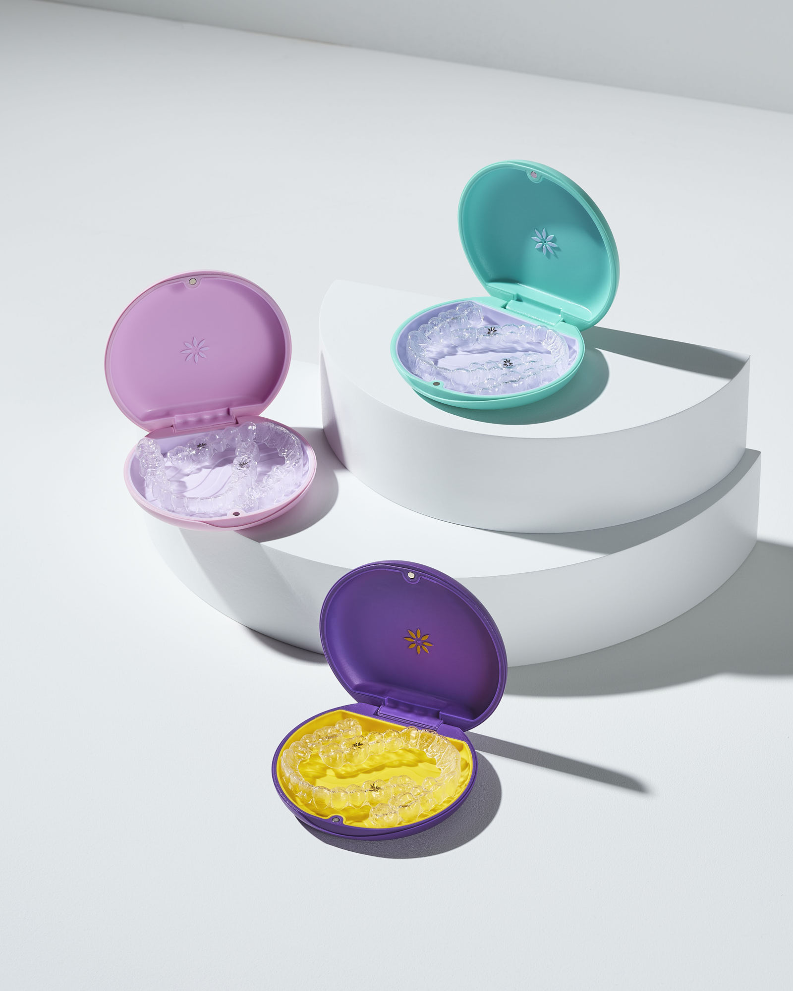 Colorful retainer cases with clear dental aligners on white background.