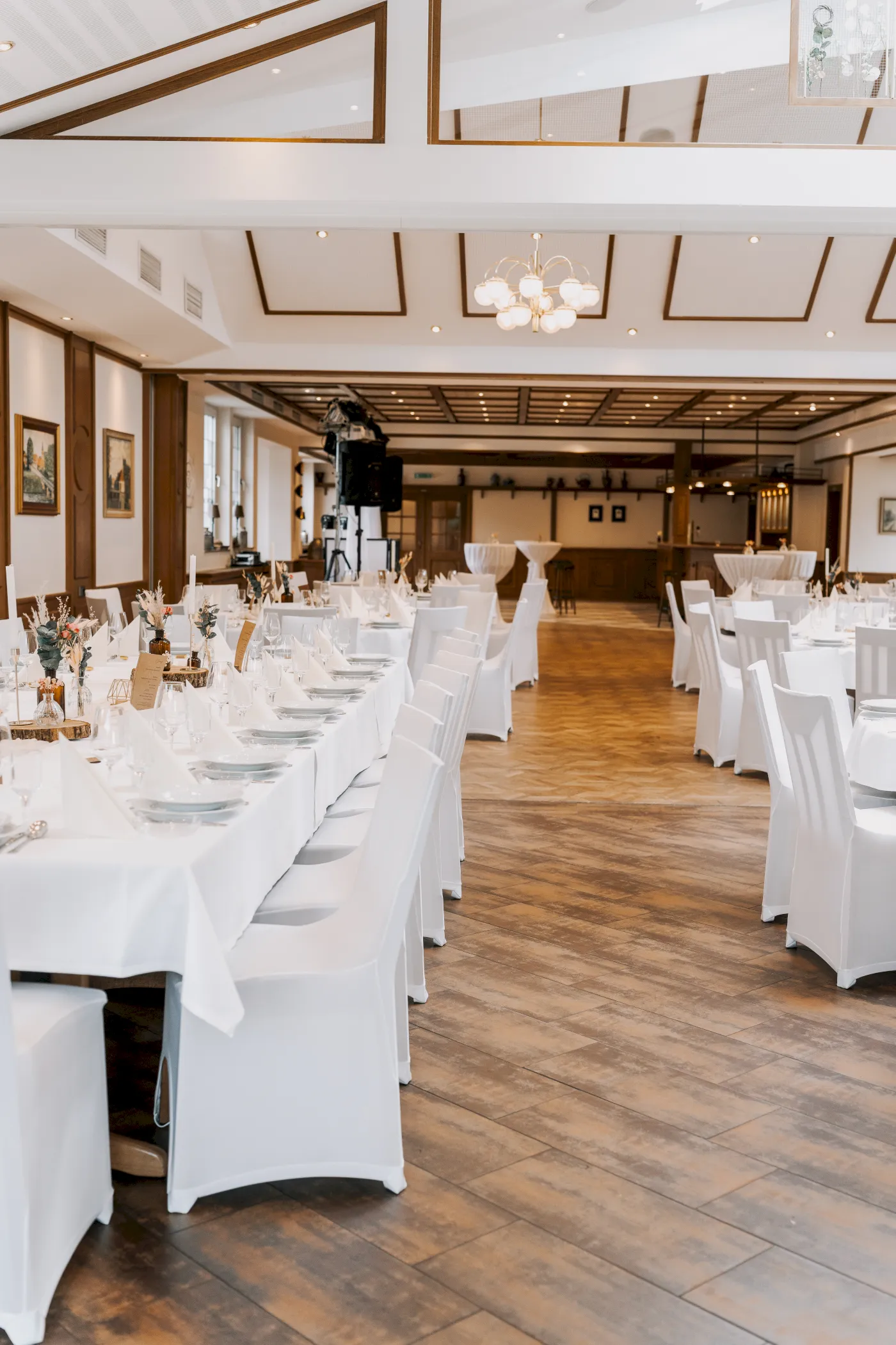 Großer Saal mit Holzboden und weißen Tischdecken, ideal für Hochzeiten oder Feiern.