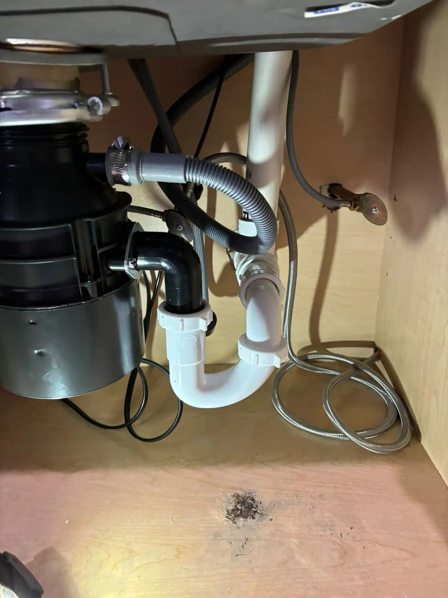 A black garbage disposal unit fully mounted under a kitchen sink, inspected during a professional garbage disposal repair.