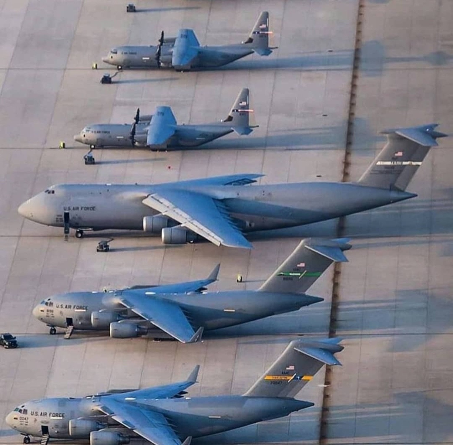 U.S. Air Force mobility aircraft, including C-130s and C-17s, parked in rows on a flight line