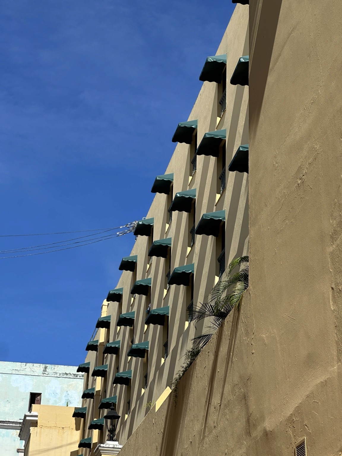 Repeating green awnings on a pale building beneath blue sky. Photograph by Pranjali Shah.