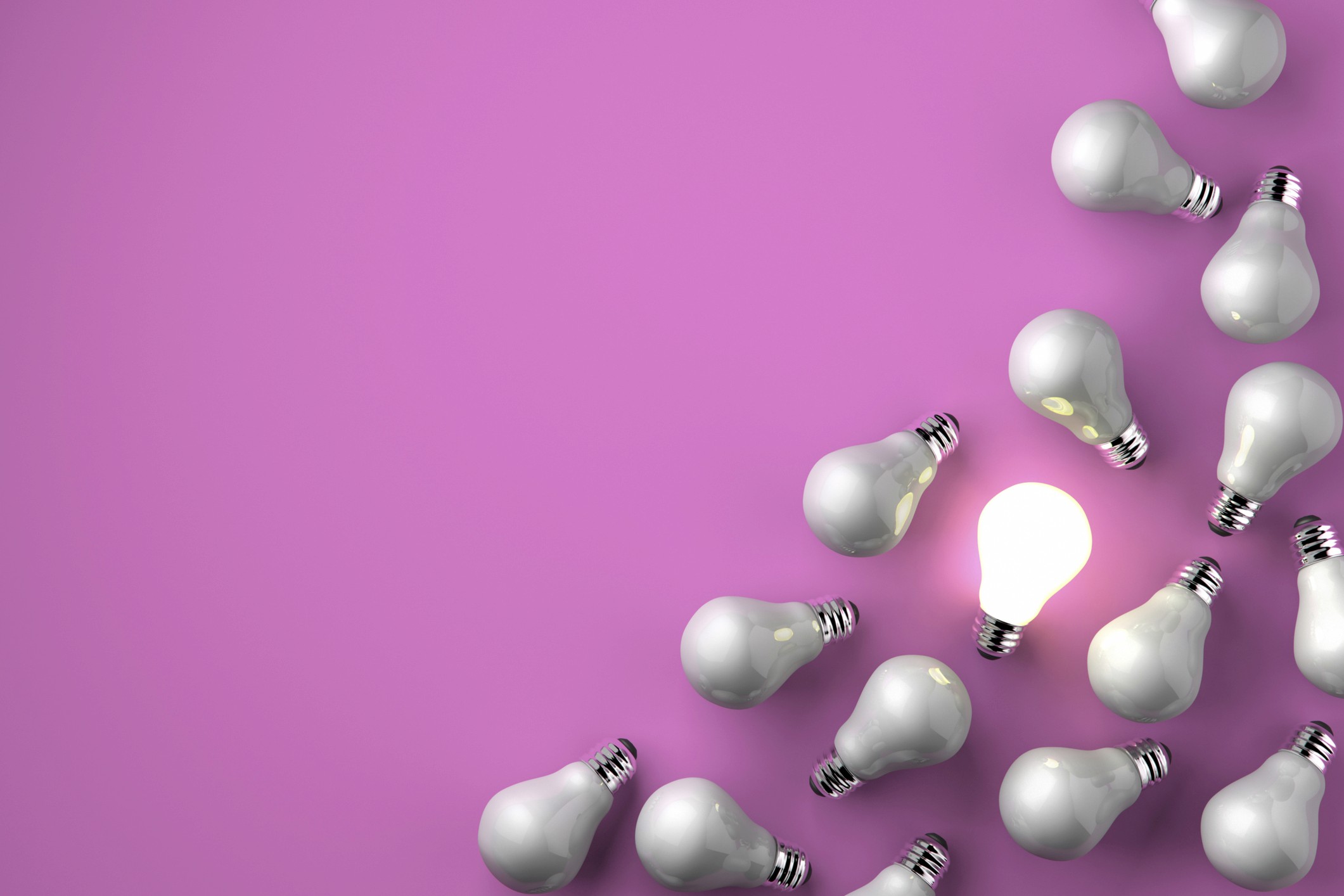 A single glowing lightbulb standing out among a group of unlit lightbulbs on a pink background, representing the concept of an outlier among the norm.